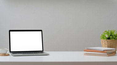 Laptop, kahve fincanı, ofis malzemeleri ve beyaz masa üzerine beyaz duvar arka planlı dekorasyonlarla kesilmiş iş yeri görüntüsü. 