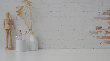 Çalışma alanını fotokopi alanı, acı fırçası, ahşap figür ve beyaz masadaki tuğla duvar zeminli seramik vazo ile kapat  