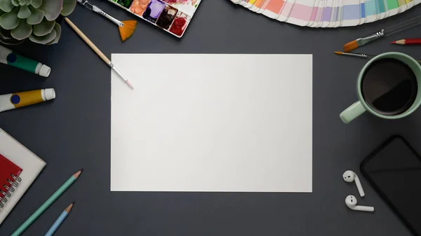 Vista dall'alto dell'area di lavoro dell'artista con carta da disegno, strumenti per dipingere, smartphone e tazzina da caffè su sfondo grigio — Foto Stock