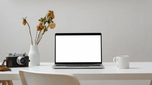 Vista cercana del espacio de trabajo con computadora portátil de pantalla en blanco, cámara, café y jarrón asado seco en una mesa de madera blanca —  Fotos de Stock