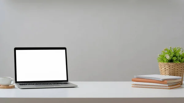 Обрезанный снимок рабочего места с макетом ноутбука, чашки кофе, канцелярские принадлежности и украшения на белом столе с белым фоном стены — стоковое фото