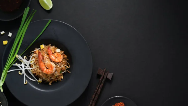 Horní pohled na Pad Thai, míchání moucha thajské nudle s krevetami, vejce, kopírovací prostor a koření v černé keramické desky na černém stole — Stock fotografie