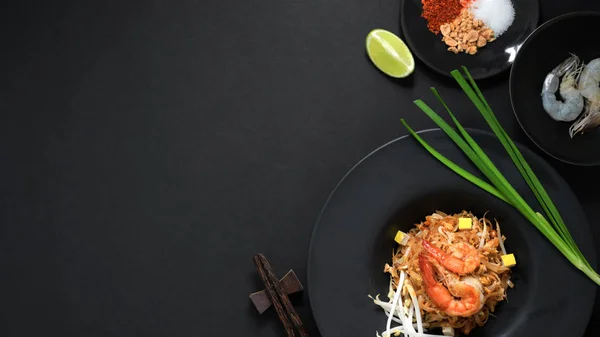 Over head shot of Pad Thai, stir fly of Thai noodle with shrimp, egg, ingredients and seasoning with copy space in black ceramic plate on black table — 스톡 사진