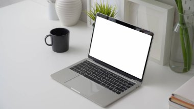 Boş ekran dizüstü bilgisayarı, ofis malzemeleri, dekorasyonlar ve beyaz masa arkasındaki kahve fincanı ile kırpılmış çalışma alanı.