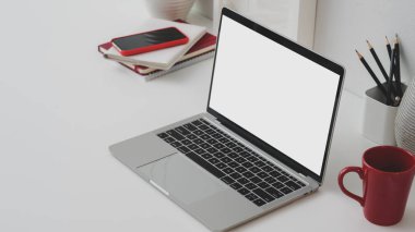 Boş ekran dizüstü bilgisayarı, ofis malzemeleri ve beyaz masa arkasında kahve fincanı olan bir çalışma alanı.