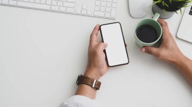 Modern çalışma alanında bilgisayar ve ofis malzemeleriyle akıllı telefon kullanan bir iş adamının genel görüntüsü.