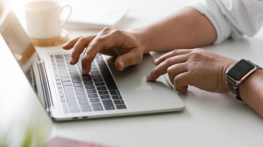 Basit bir çalışma alanında iş adamının kahve fincanı ve ofis malzemeleriyle bilgisayarda yazı yazmasının yan görüntüsü
