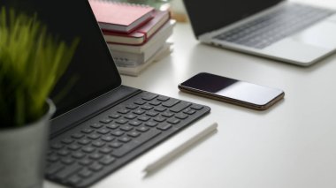 Dijital tablet, akıllı telefon, dizüstü bilgisayar, fotokopi alanı ve diğer ofis malzemelerini pratik iş yerindeki beyaz masa arkaplanında kırpılmış çekimler