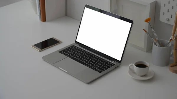 Cropped shot of workspace with blank screen laptop, office supplies, decorations and red coffee cup on white desk background