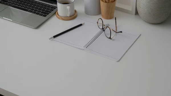Обрезанный снимок рабочего места с ноутбуком, ноутбуком, копировальным пространством, офисными принадлежностями и кофейной чашкой на белом фоне стола — стоковое фото