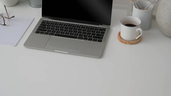 Fotografía recortada del lugar de trabajo con computadora portátil, espacio de copia, suministros de oficina y taza de café sobre fondo de escritorio blanco — Foto de Stock