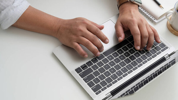 Вид сверху бизнесмена, сидящего на ноутбуке в простом рабочем пространстве с чашкой кофе и канцелярскими принадлежностями
