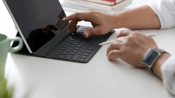 Foto seorang pengusaha mengetik di papan tik tablet di tempat kerja sederhana dengan cangkir kopi dan perlengkapan kantor — Stok Foto