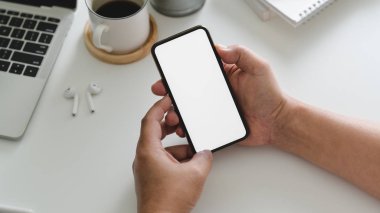 Beyaz masa arkasında diğer ofis malzemeleriyle birlikte akıllı telefon tutan işadamının görüntüsü.
