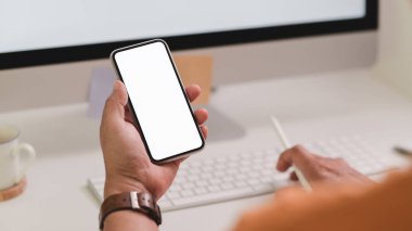 Modern çalışma alanında bilgisayarda yazarken akıllı telefon tutan erkek serbest çalışanın görüntüsünü kapat