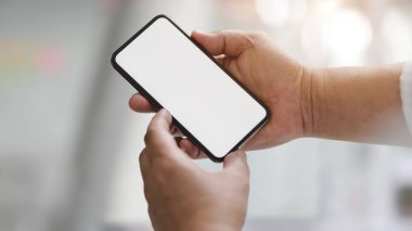 İş adamının atölyede akıllı telefon tutarken görüntüsü bulanık beyaz masa arkasında diğer ofis malzemeleriyle birlikte.
