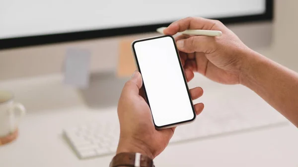 Vista de perto do freelancer masculino segurando smartphone enquanto trabalhava no computador no espaço de trabalho moderno — Fotografia de Stock