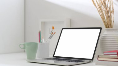 Boş ekran dizüstü bilgisayar, kahve fincanı, boya fırçası ve beyaz masa süslemeleri ile basit sanatçı çalışma alanının kırpılmış görüntüleri 
