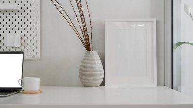 Beyaz masadaki çerçeve ve seramik vazo ile modern kopyalama alanının görünümünü kapat 