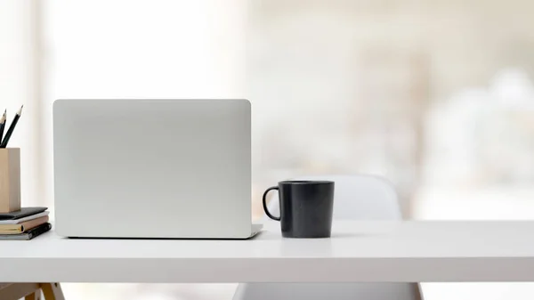 Vista cercana del espacio de trabajo con computadora portátil, suministros de oficina, taza de café y espacio de copia en el escritorio blanco —  Fotos de Stock