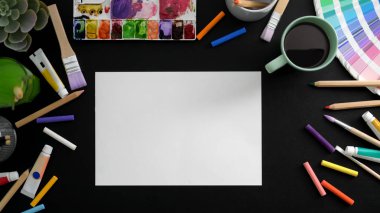 Eskiz kağıdı, boyama araçları ve kahve fincanı ile sanatçı çalışma alanının üst görünümü 