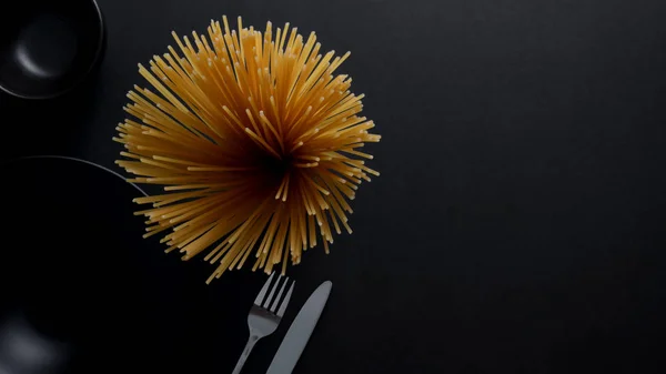 Bovenaanzicht van Geel lange spaghetti op zwart bord en bestek — Stockfoto