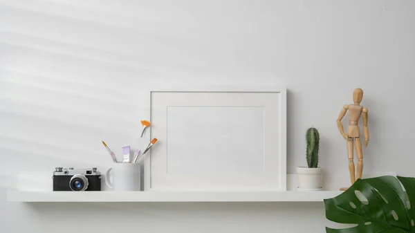 Vue rapprochée du cadre maquette, de la caméra et des décorations sur étagère blanche avec fond mural blanc — Photo