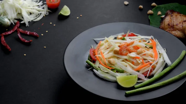 Vista de cerca de ensalada de papaya en plato negro, parrilla de pollo en taro verde e ingredientes — Foto de Stock