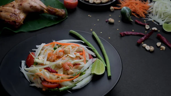 Foto recortada de ensalada de papaya en plato negro, parrilla de pollo en taro verde e ingredientes — Foto de Stock