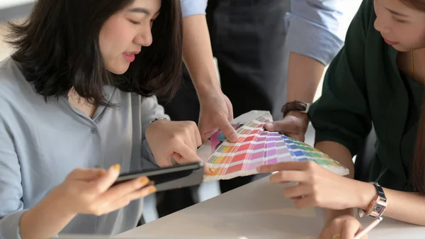 Close up view of young professional designer team consulting on their project with smartphone and coloured swatch in simple co working space — Stock Photo, Image