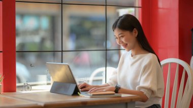 Portrait of adorable college girl working on her assignment with tablet in modern co-working space 