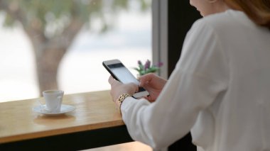 Basit bir kafede otururken akıllı telefondan mesaj atan bir kadının görüntüsü.