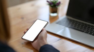 Ahşap masanın üzerinde boş ekran akıllı telefon tutan bir kadının kırpılmış görüntüsü. 