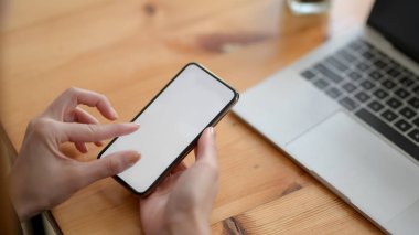 Ahşap masadaki boş ekran akıllı telefona dokunan bir kadının yakın görüntüsü