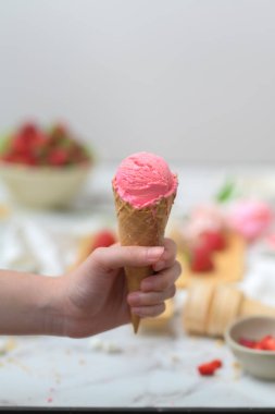 Çilekli dondurma külahını tutan bir kızın kırpılmış görüntüsü. 