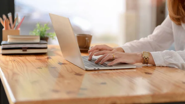 Vista laterale di una donna che digita sul computer portatile sulla scrivania di legno mentre è seduta in un posto di lavoro semplice — Foto Stock