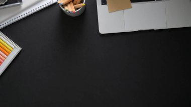 Dizüstü bilgisayarı, acı aletleri ve diğer malzemeleri olan sanatçının çalışma alanının en üst görünümü siyah masanın üzerinde 