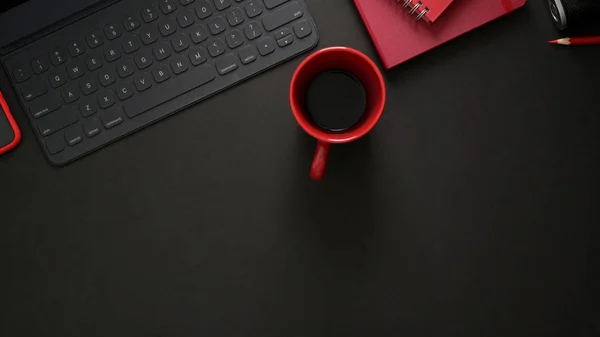 Top άποψη του κομψού χώρου εργασίας με ασύρματο πληκτρολόγιο, προμήθειες γραφείου, αντίγραφο χώρου και κόκκινο φλιτζάνι καφέ σε μαύρο τραπέζι — Φωτογραφία Αρχείου