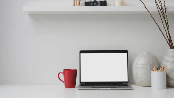 Oříznutý záběr pracoviště s prázdnou obrazovkou notebook, červený šálek kávy, dekorace na bílém stole — Stock fotografie