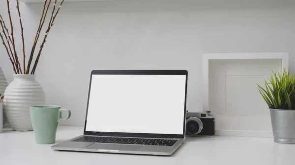 Captura recortada del lugar de trabajo con la computadora portátil de pantalla en blanco, marco, decoraciones y cámara en el escritorio blanco —  Fotos de Stock