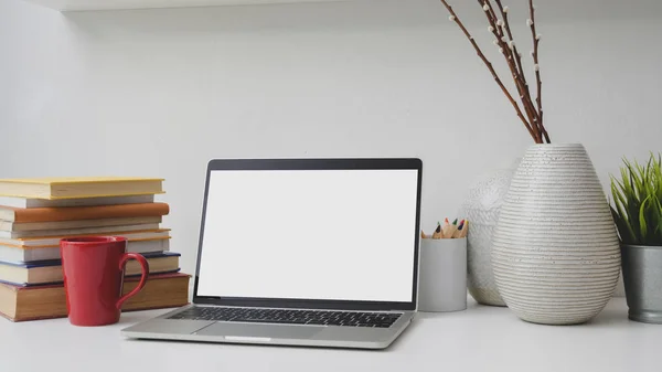 Captura recortada de lugar de trabajo con computadora portátil de pantalla en blanco, libros, decoraciones y taza de café rojo —  Fotos de Stock