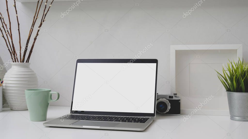 Cropped shot of workplace with blank screen laptop, frame, decorations and camera on white desk 
