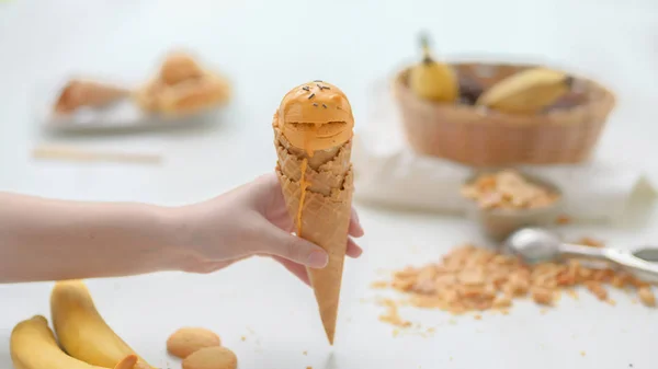 Nahaufnahme eines Mädchens mit Erdnussbutter-Bananen-Eiskegel auf weißem Tischhintergrund — Stockfoto