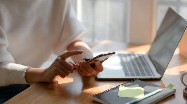 Basit bir iş yerinde rahatlarken akıllı telefon kullanan üniversiteli genç bir kızın görüntüsü. 