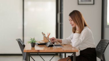Dijital tablet üzerinde çalışan kadın serbest çalışanın yan görünüşü basit bir çalışma alanında ahşap masa üzerinde kırtasiye malzemesi