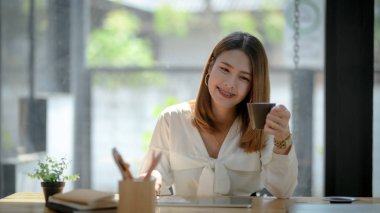 Bir kadının basit bir iş yerinde otururken elinde kahve fincanı tutmasını yakından izlerim. 