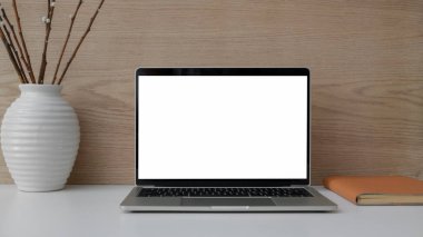 Modern kırsal duvarlı beyaz masa üzerinde dizüstü bilgisayar, defter ve seramik vazo ile basit iş yeri görünümünü kapat