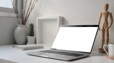 Boş ekran dizüstü bilgisayarı, ahşap figürü ve pencerenin yanındaki beyaz masanın üzerindeki süslemelerle en az iş yeri görüntüsü.