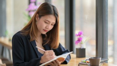 Yan taraftaki kahve dükkanının bar taburesinde otururken bir kadının deftere bir fikir yazması. 