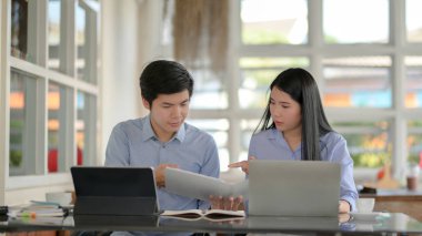 İki iş adamının projeleri hakkında tablet, dizüstü bilgisayar ve diğer ofis malzemeleriyle basit ortak çalışma alanları hakkında brifing vermelerine yakından bakın.